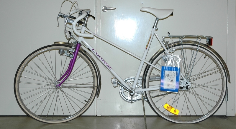 a) Lila/vit 5-växlad Crescentcykel. Bockstyre med vit lindning. Två handbromsar samt fotbroms. Vit sadel märkt "Iscaselle". Reflex på bakhjul, ej fram. Märkning: Crescent. Sports Bike. Crescentemblem fram. 1990-tal. b) Instruktionsbok. Monark och Crescentcyklar 1991.