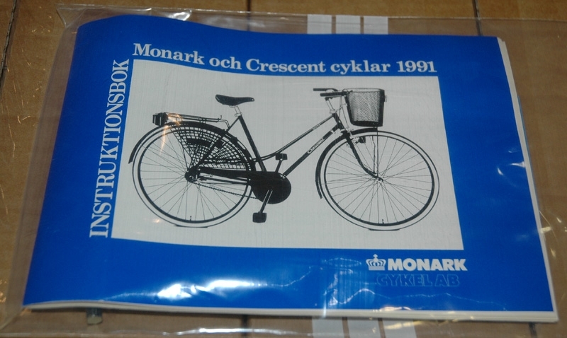 a) Lila/vit 5-växlad Crescentcykel. Bockstyre med vit lindning. Två handbromsar samt fotbroms. Vit sadel märkt "Iscaselle". Reflex på bakhjul, ej fram. Märkning: Crescent. Sports Bike. Crescentemblem fram. 1990-tal. b) Instruktionsbok. Monark och Crescentcyklar 1991.