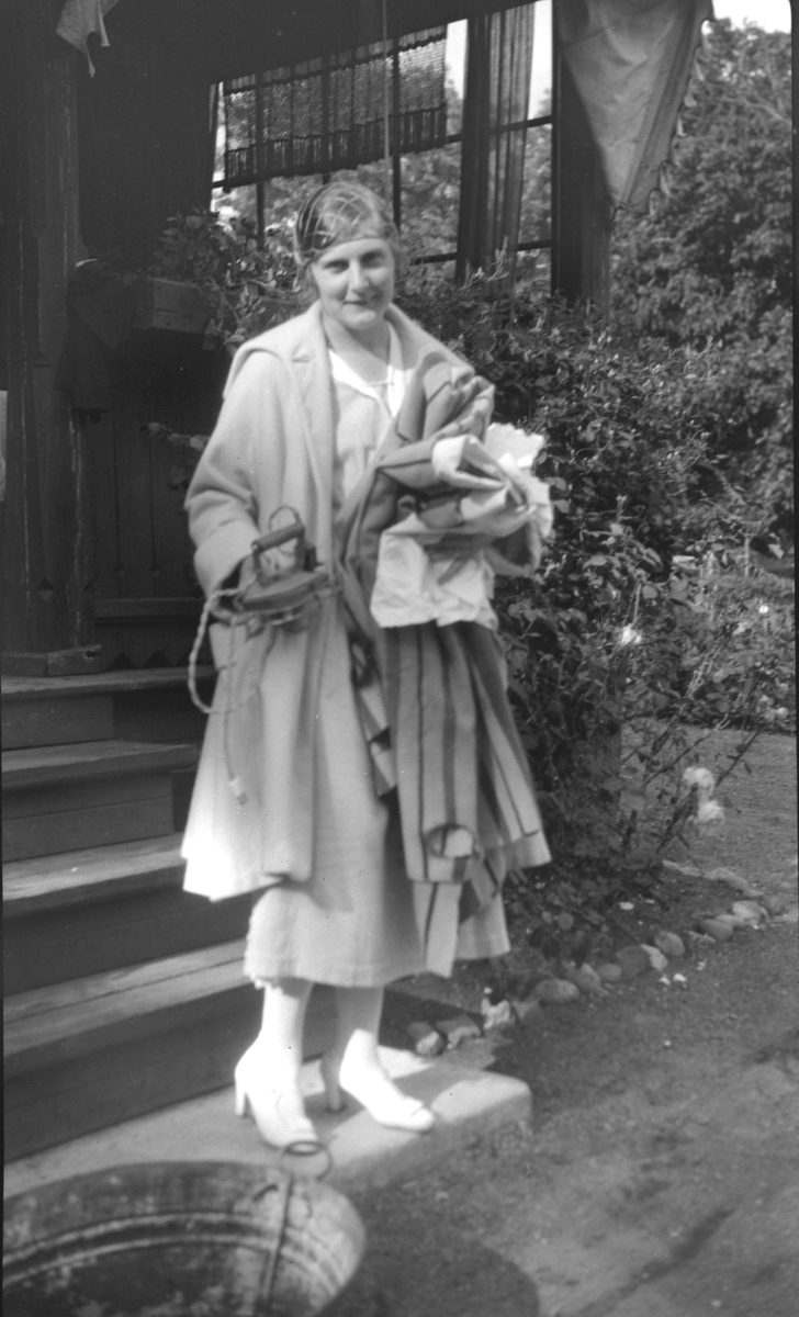 Med et strykejern i hånden står Hilda Sundt utenfor sin svoger Halfdans Sundts hus i Stavern.