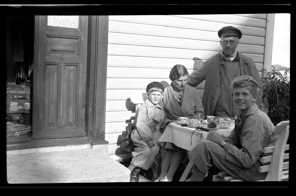 Rolf sr. og Hilda Sundt og deres sønner Lars Peter og Rolf jr. sitter ved et bord utenfor et hus, Naudodden, Farsund. Fotografert 1936.