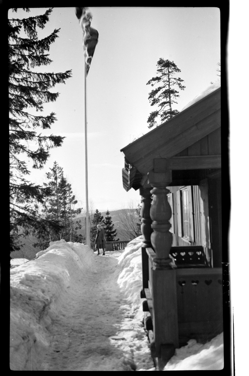 En dame står i snø ved flaggstangen, Villa Knyggen. Fotografert 1918-1919.