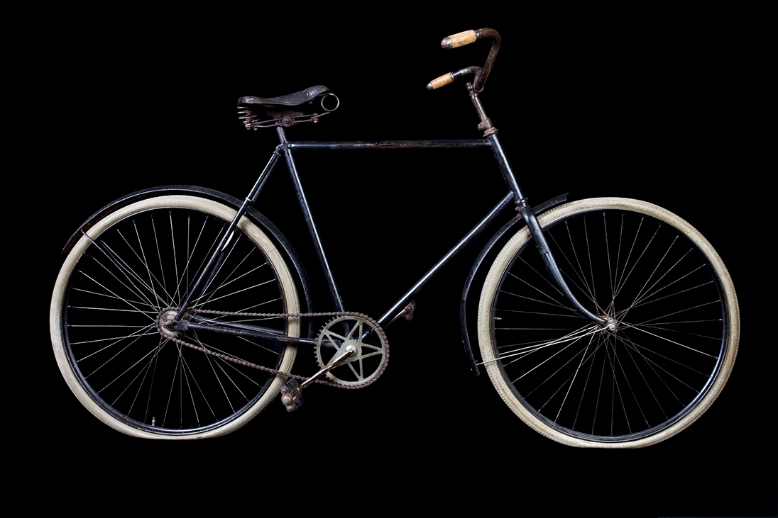 Cykel av stålrör. Diamond-ram. Spiralfjädrad lädersadel. Styrhandtag av trä. Stålfälgar på suspensionsekrar. Hel vev. Frihjulsnav med broms. Stänkskärmar, av vilka den främre löper framom gaffeln. Svart. Sadelfjädrar, styre, vevparti och skärmstag förnicklade.