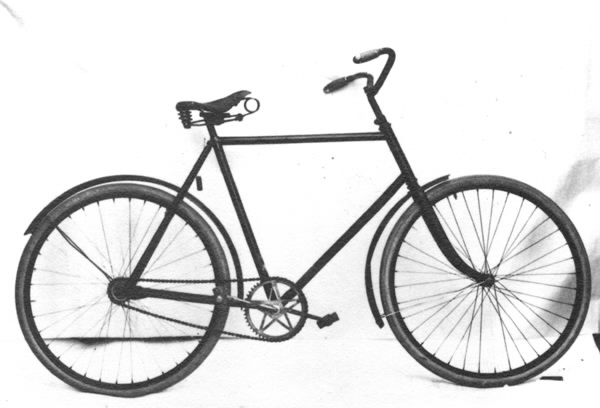 Cykel av stålrör. Diamond-ram. Spiralfjädrad lädersadel. Styrhandtag av trä. Stålfälgar på suspensionsekrar. Hel vev. Frihjulsnav med broms. Stänkskärmar, av vilka den främre löper framom gaffeln. Svart. Sadelfjädrar, styre, vevparti och skärmstag förnicklade.