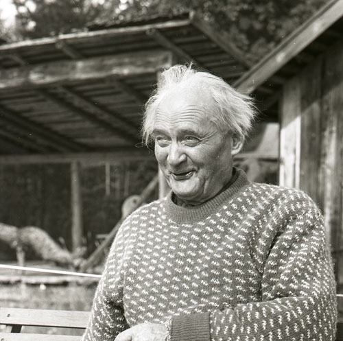 Författaren Albert Viksten sitter vid ett bord utomhus framför en träbyggnad. Han ler och berättar fiskehistorier, 19 augusti 1962.