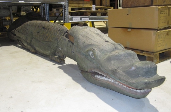 Alligator/krokodil med ett huvud och två sidor, som omslutit stäven. Öppen käft med sammanhängande tandrader och rombformade fjäll på ryggen. Målad i grönt och gult. Krokodilen består av flera delar, varav stora delar tidigare varit rejält angripna av röta. Huvud och höger sida är bäst bevarade.