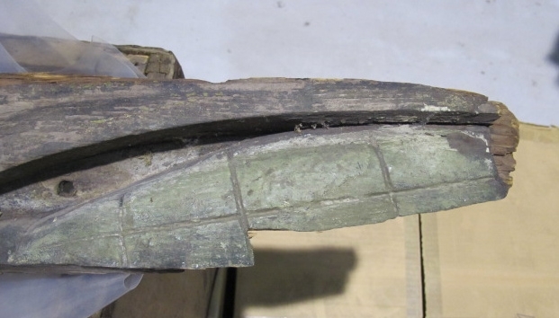 Alligator/krokodil med ett huvud och två sidor, som omslutit stäven. Öppen käft med sammanhängande tandrader och rombformade fjäll på ryggen. Målad i grönt och gult. Krokodilen består av flera delar, varav stora delar tidigare varit rejält angripna av röta. Huvud och höger sida är bäst bevarade.