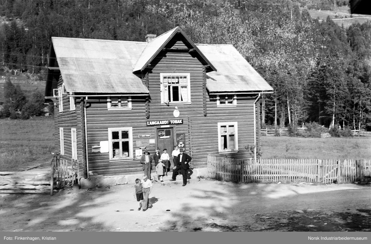 Mennesker stående foran O.T. Dale landhandel i Tinn Austbygd. Skilt med påskrift Langaards tobak over inngangsdør.