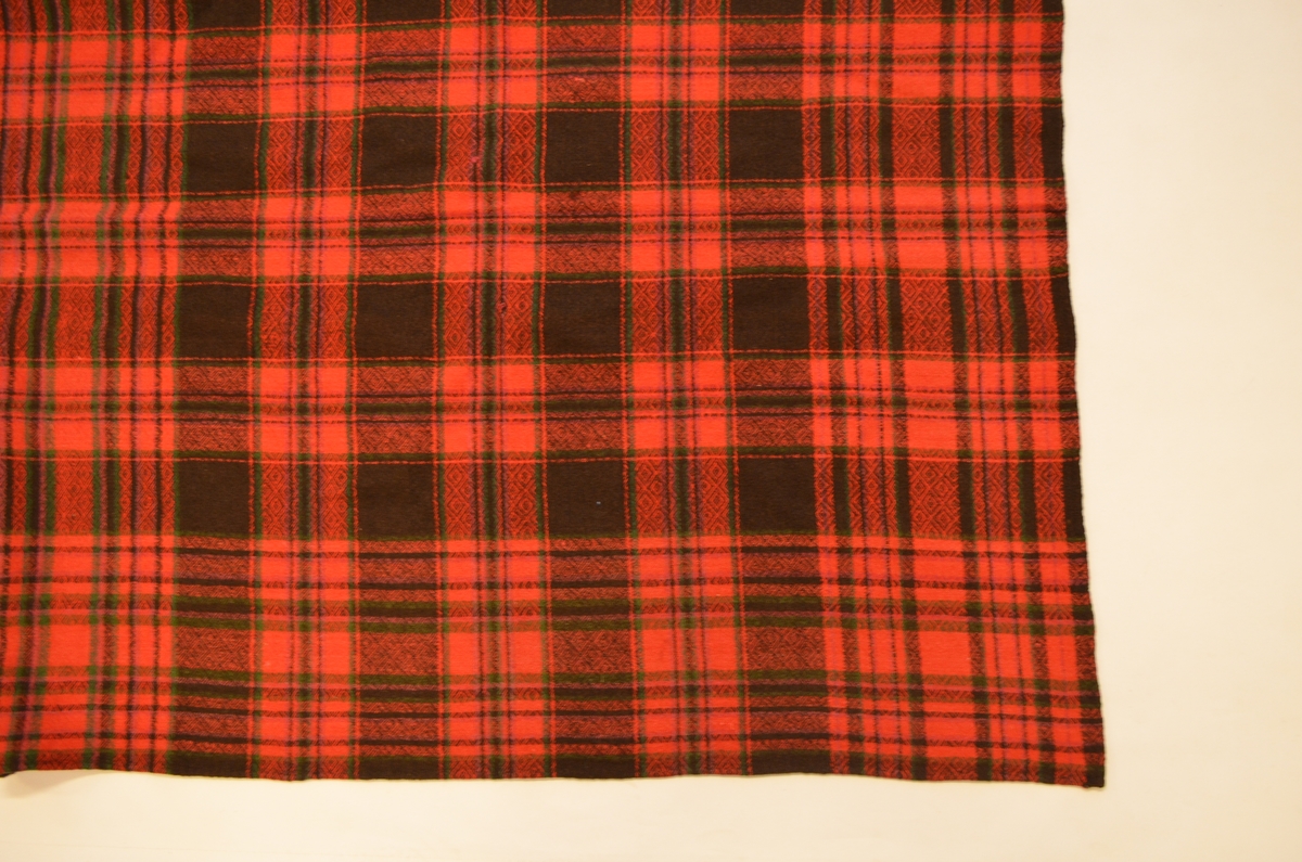 Sjal i ruta raudt, sauesvart og flaskegrønt ullgarn. Mønstervove i odd og vend. Falda for hand rundt kantane.