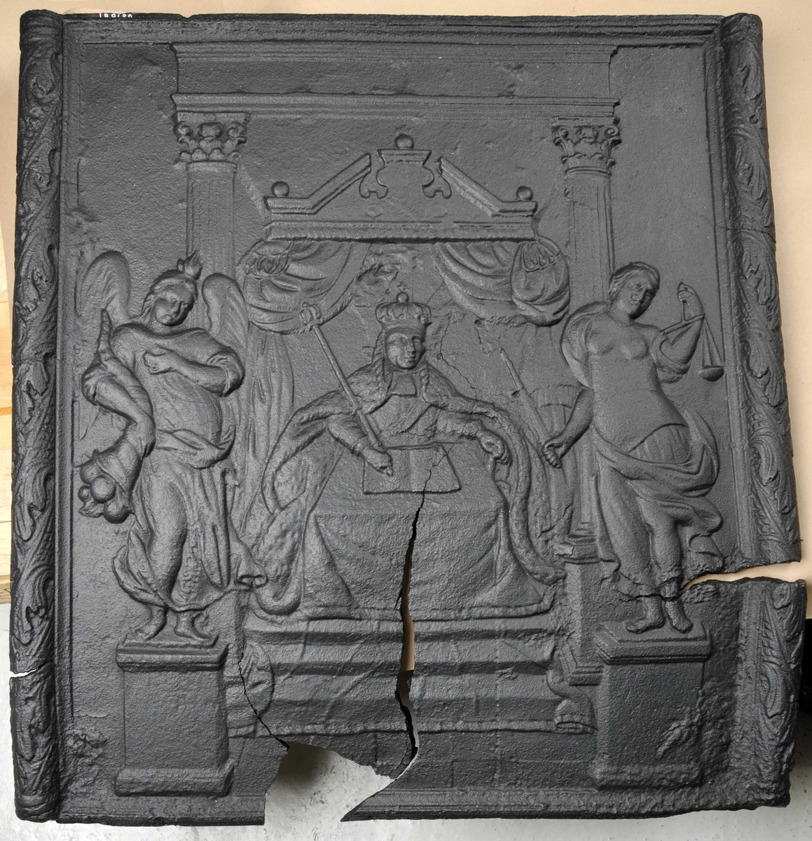 I sentrum sit ein konge med septer, til venstre ein engel med overflødighetshorn. Til høgre ein figur med vekt i eine handa og sverd i andre handa. Kongen sit i ei trone.