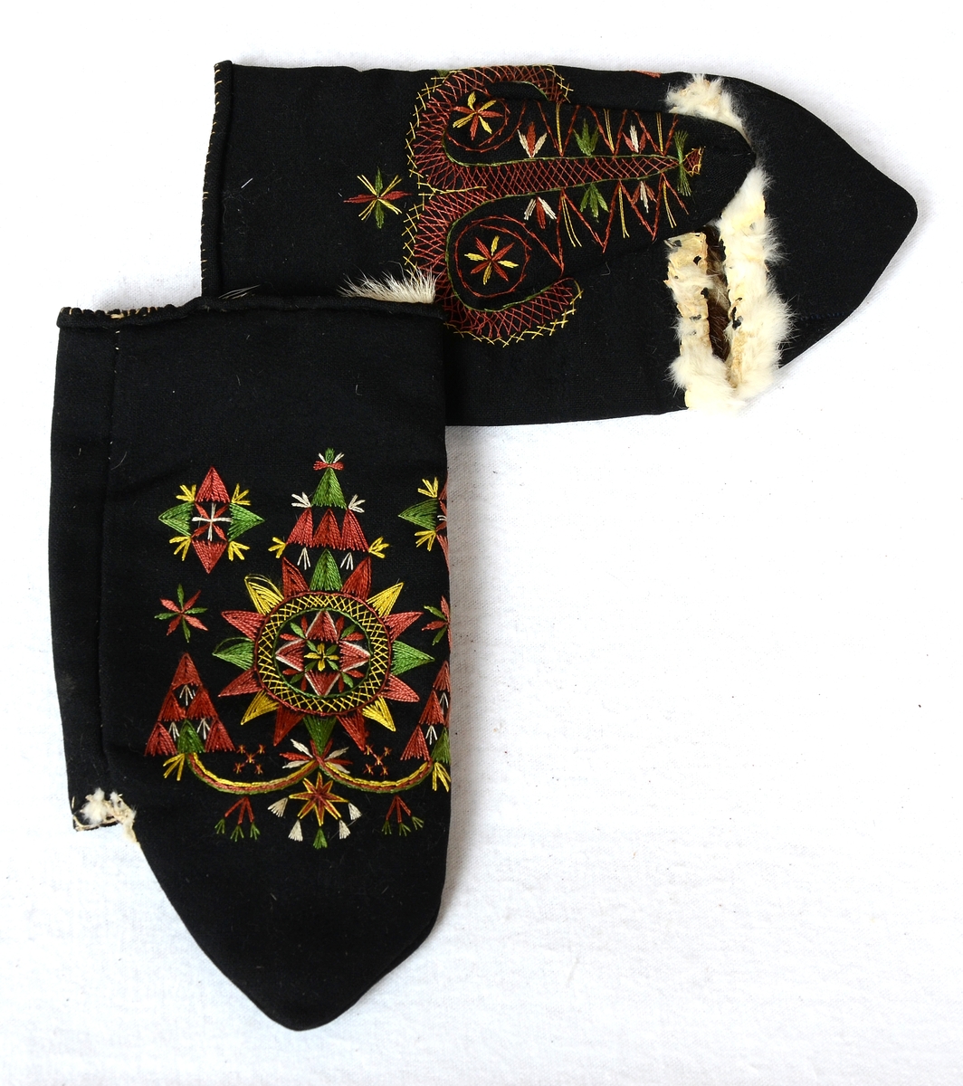 Svarta vinterkyrkvantar. Skinnfodrade med renskinn. Broderi utfört i stjälkstygn, plattsöm och flätsöm med silkegarn i grönt, brunt, vitt och gult. Inuti handen och på tummen öppningar kantade med mjukt vitt skinn. Öppningarna är till för kunna bläddra i psalmboken.