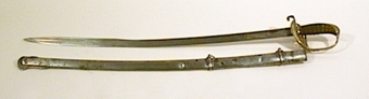 Infanteriofficerssabel. Fästenas beslag är av förgylld mässing och parerplåten är dekorerad med genombrutna ornament. Kaveln är klädd med svärtat fiskskinn, med åtta refflor i vars bottnar tvinnade mässingstrådar anbringats. . På klingans flatsidor finns etsade och delvis förgyllda ornament.