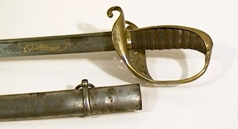 Infanteriofficerssabel. Fästenas beslag är av förgylld mässing och parerplåten är dekorerad med genombrutna ornament. Kaveln är klädd med svärtat fiskskinn, med åtta refflor i vars bottnar tvinnade mässingstrådar anbringats. . På klingans flatsidor finns etsade och delvis förgyllda ornament.