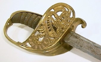 Infanteriofficerssabel. Fästenas beslag är av förgylld mässing och parerplåten är dekorerad med genombrutna ornament. Kaveln är klädd med svärtat fiskskinn, med åtta refflor i vars bottnar tvinnade mässingstrådar anbringats. . På klingans flatsidor finns etsade och delvis förgyllda ornament.