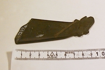 Fragment av kniv, gråbrun skiffer med ett tvärgående ljust band. Endast skaftändan återstår. Denna har formen av ett älghuvud, väl slipad.