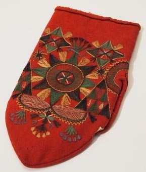Röd vinterkyrkvante som fodrats med grått skinn. Broderi utfört i stjälkstygn, plattsöm och flätsöm med silkegarn i blått, brunt, svart, vitt och gult. Inuti handen och på tummen finns öppningar, kantade med mjukt vitt skinn, som är till för att kunna bläddra i psalmboken.