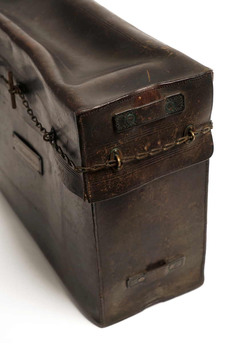 Veske av lær med 9 messingbøyler og to messinglenker for låseanordning. Låsepinne av tre. (Denne ligger i vesken)