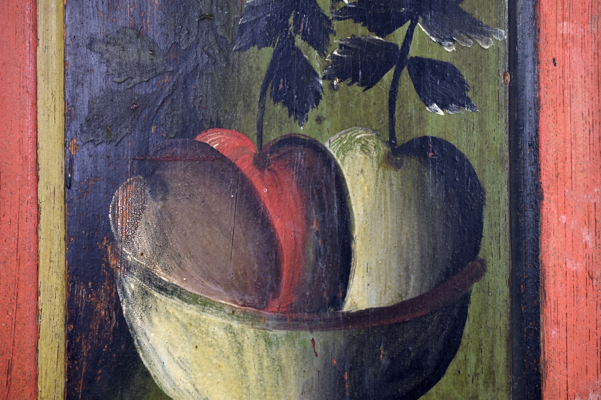 Rektangulär fyllning till skåpsdörr. Röd kant runt dörrfälten där en skål med tre äpplen är avbildade.