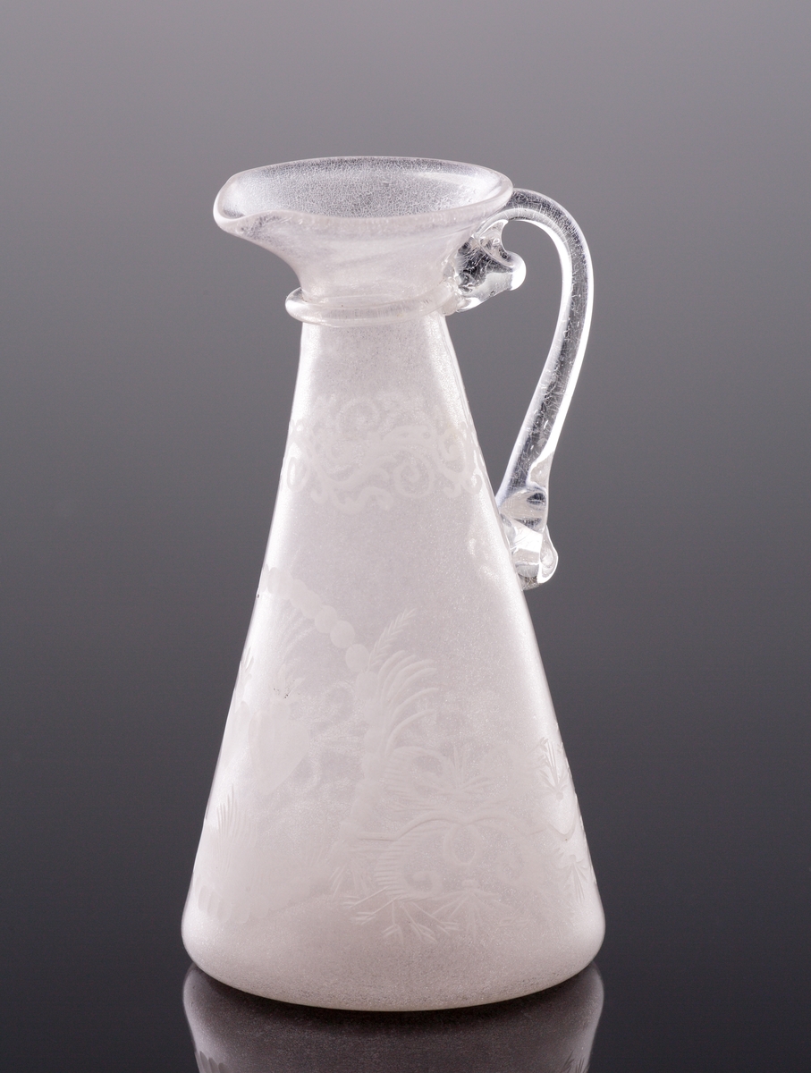 Kanna. 
Konande modell med hänkel och graverad dekor av bladrankor, två brinnande hjärtan m.m.
Mynningen utvikt med en formad pip. Under mynningen en påklippt ring.