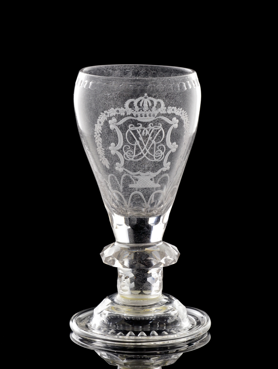 Pokal av glas. Lock saknas. 
Graverad dekor av kungligt spegelmonogram: "FR"* i kartusch under krona. 

*"FR" (Fredericus Rex= Fredrik I av Sverige, reg. 1720-1751).