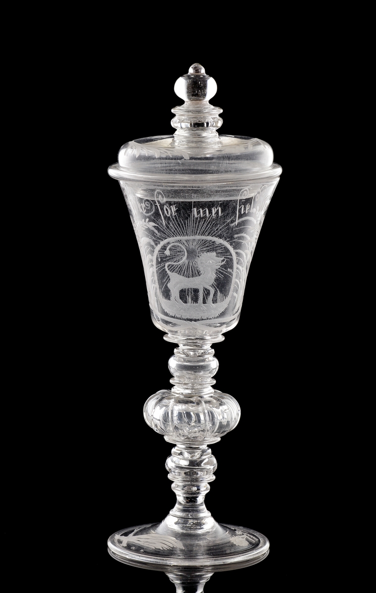 Pokal med lock i venetiansk stil. 
Graverat mönster i form av ett stående lejon m.m.. Text: "Jag Lefwer för mei Sjelfwer". 
Invikt kant på foten.