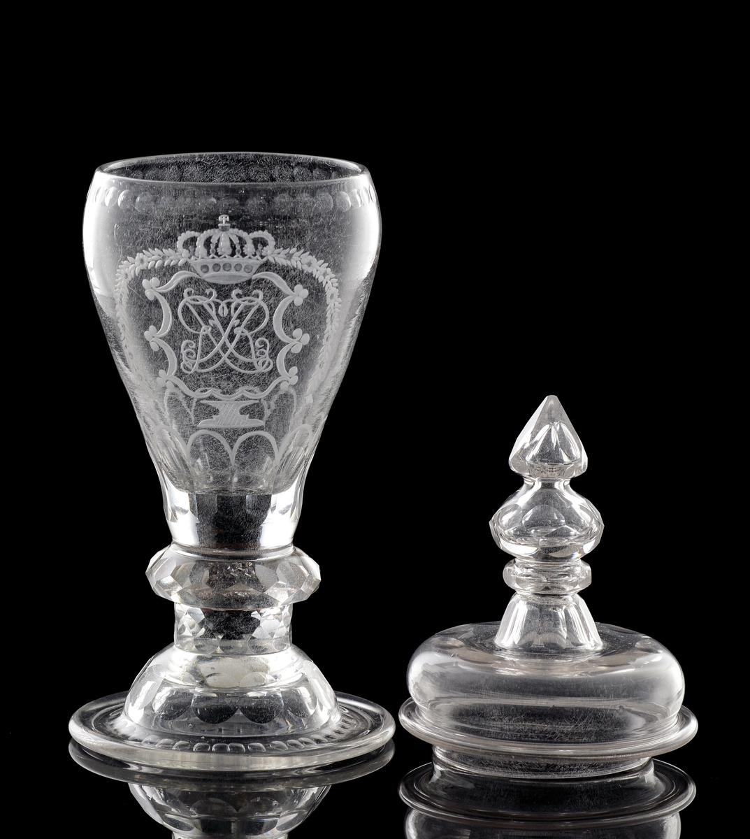 Pokal av glas, med lock. 
Slipat och graverat mönster med kungligt spegelmonogram: "FR"* i kartusch under krona. Invikt kant på foten.

*"FR" (Fredericus Rex= Fredrik I av Sverige, reg. 1720-1751).
