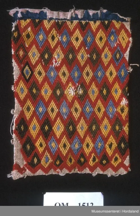 Bringeklut brodert med diamantmønster i raud, blå, gul og brun farge.