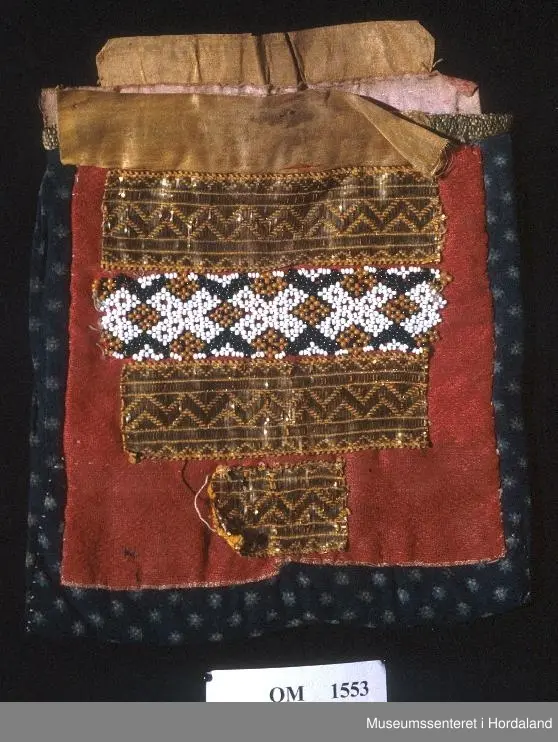 Bringeklut samansett av border på tvers, montert på raud ulldamask. Øvst ein gul silkekvarde montert utanpå ein krokakvarde. Bringekluten er forlenga i høgda frå baksida, og har eit silkeband i toppen som kjem over det andre. Bordene er to metallband med perlenettbord mellom. Nedst ein liten bit av same gullband. Mørkeblått klede til bakstoff.