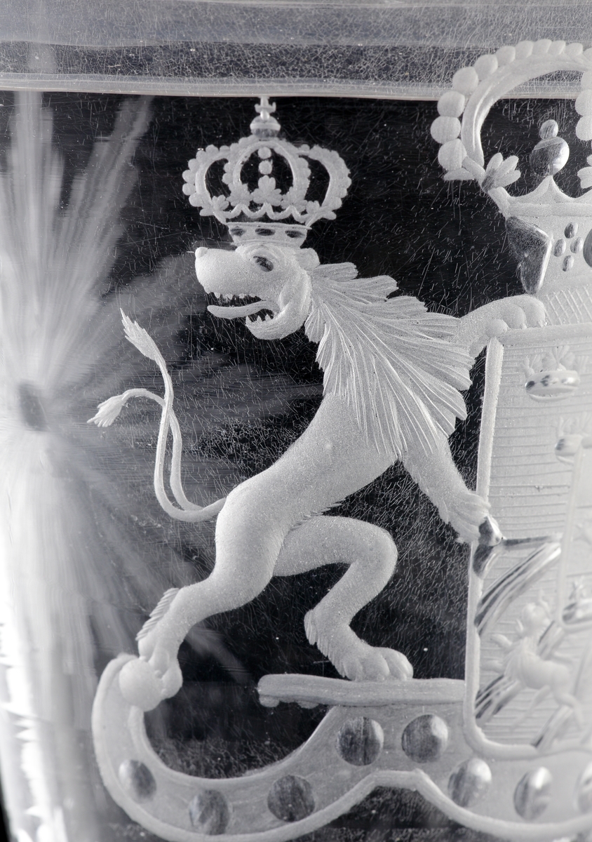 Pokal av glas, med lock.
Försedd med graverad dekor i form av Sveriges riksvapen* under kunglig krona, m.m.

*Såsom det var utformat under Fredrik I:s tid (reg. 1720-1751).