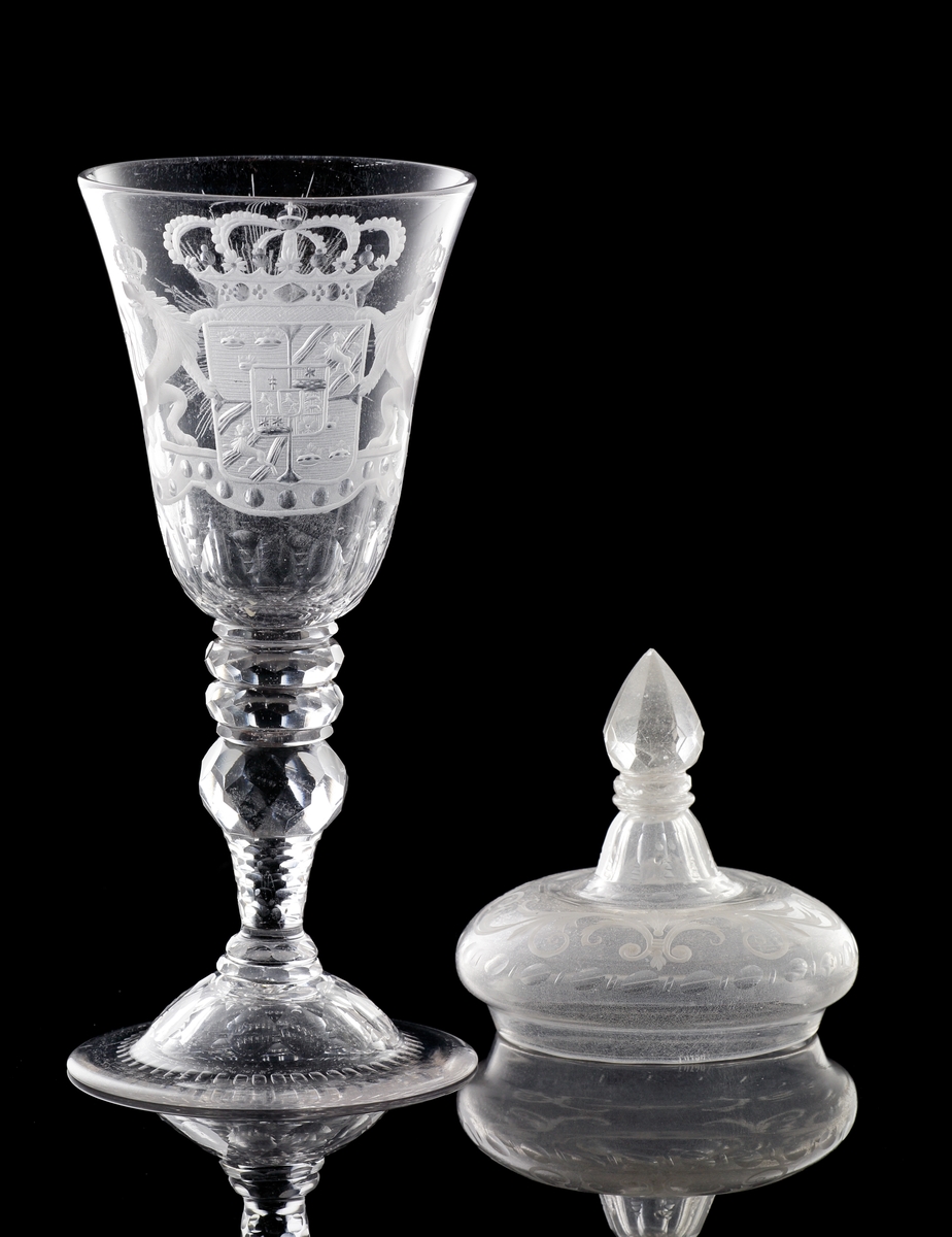 Pokal av glas, med lock.
Försedd med graverad dekor i form av Sveriges riksvapen* under kunglig krona, m.m.

*Såsom det var utformat under Fredrik I:s tid (reg. 1720-1751).