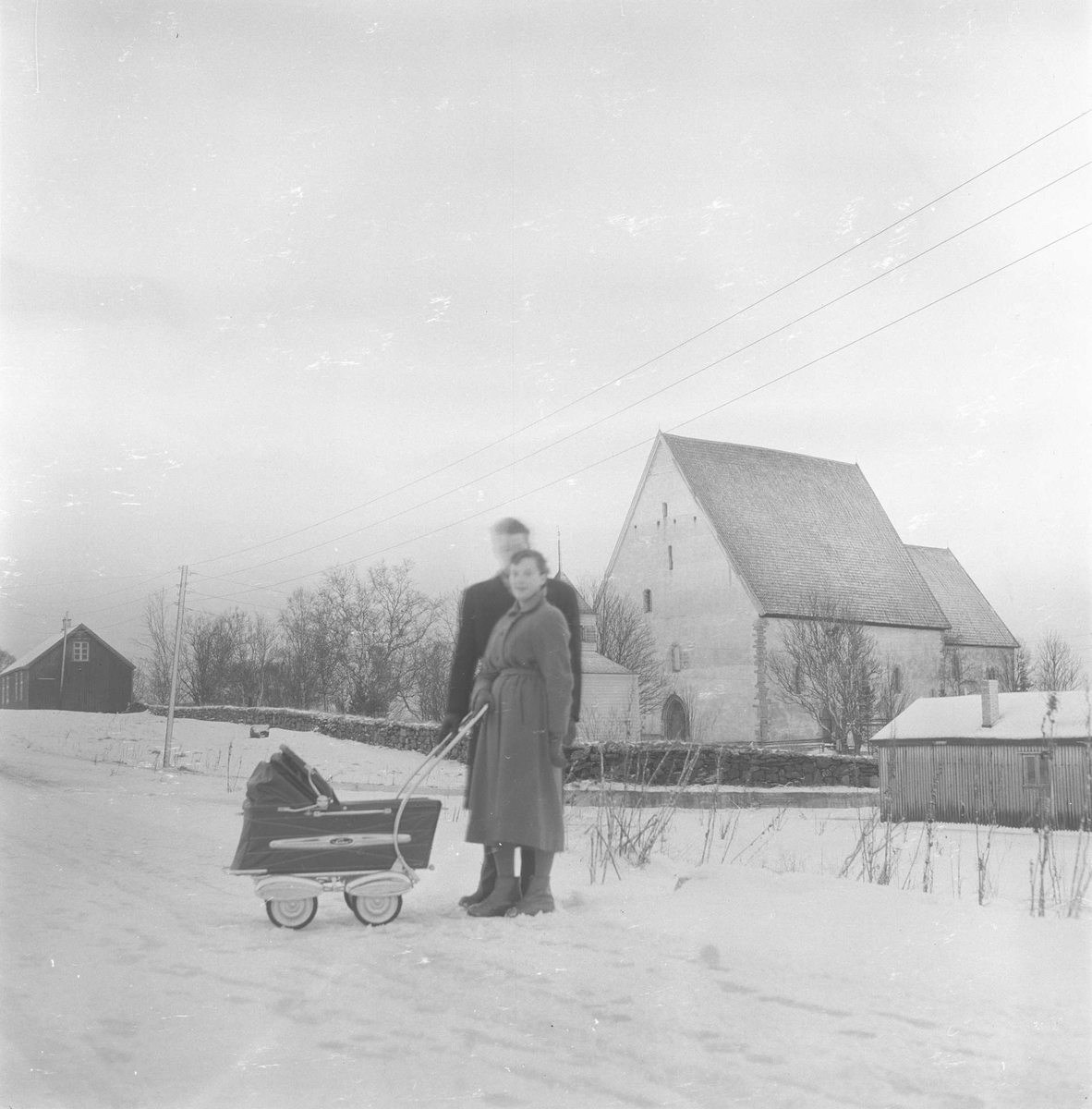 Par med barnevogn. Trondeneskirka i bakgrunnen, brakke til høyre.