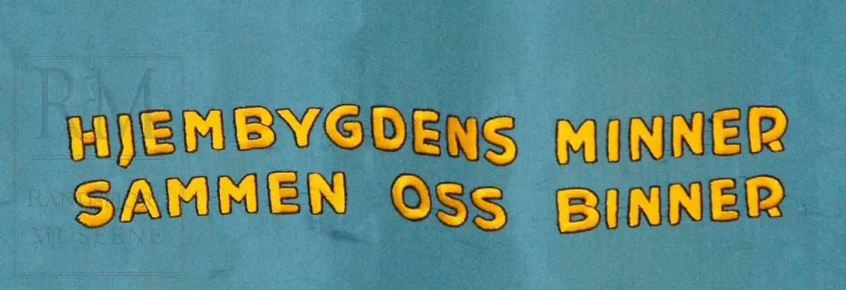 Fane; motiv og skrift på blå bunn. Skrift og possement i gull. Bæresele. Tre spyd. Brodert motiv på fremside: Utsikt fra Halvdanshaugen på Hadeland Folkemuseum, dynnasteinen i forgrunn, Tingalstad gamle kirke i bakgrunn. Bakside: Mariakirken og Nikolaikirken på Granavollen