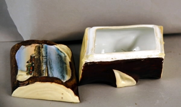 Ask med lock, porslin till förvaring av smycken. Rombisk i form av en avsågad ekstock. På locket infälld bild av "VARBERGS FÄSTNING" i färg.