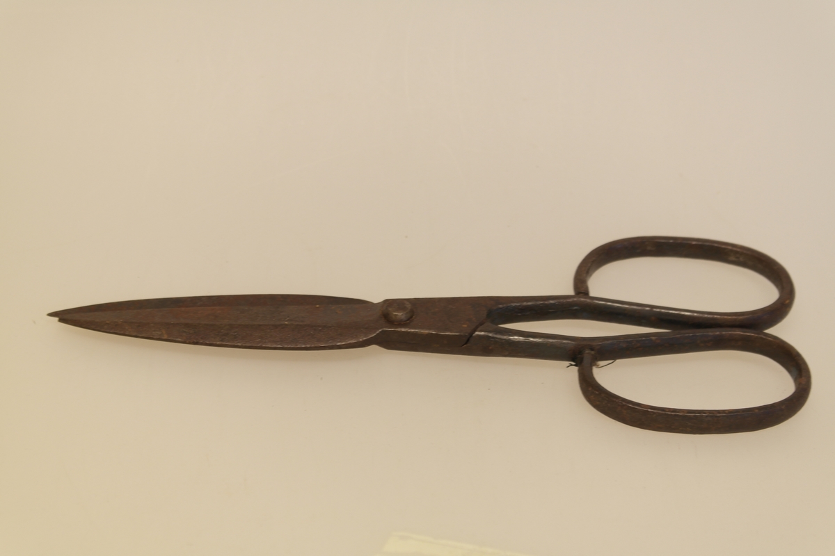 Sauesaks i smidd jern. Smidd i ett stykke. Produsentstempel på midtpartiet: motiv av en vær, samt firmanavn.