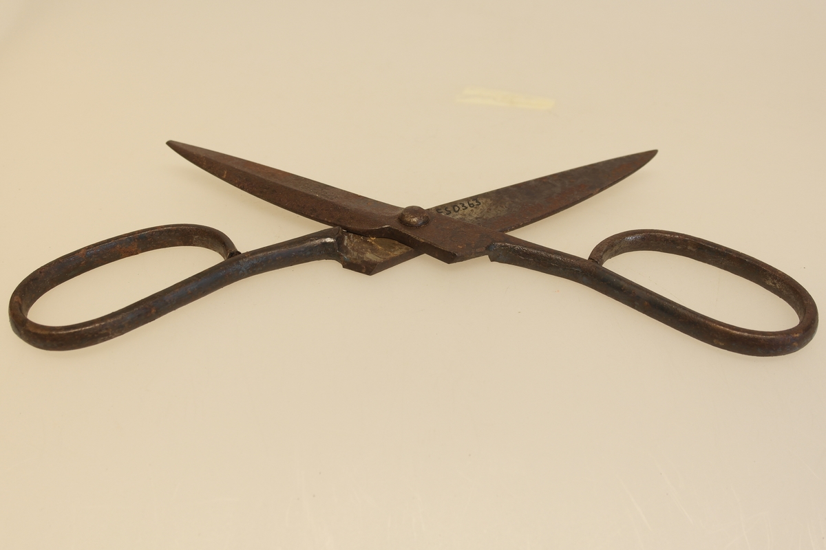 Sauesaks i smidd jern. Smidd i ett stykke. Produsentstempel på midtpartiet: motiv av en vær, samt firmanavn.