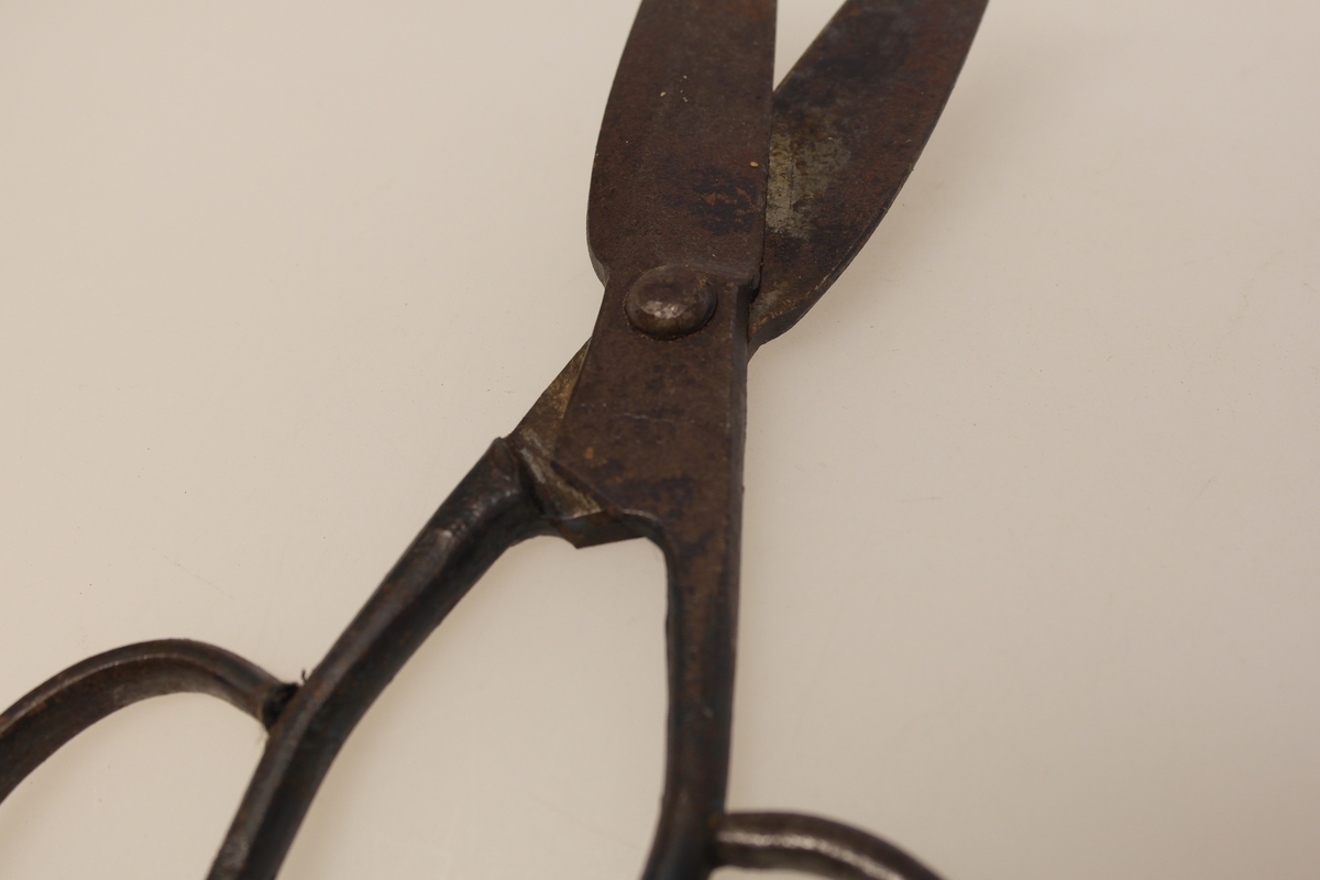 Sauesaks i smidd jern. Smidd i ett stykke. Produsentstempel på midtpartiet: motiv av en vær, samt firmanavn.