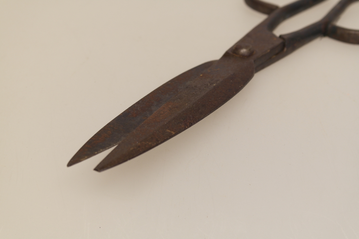 Sauesaks i smidd jern. Smidd i ett stykke. Produsentstempel på midtpartiet: motiv av en vær, samt firmanavn.