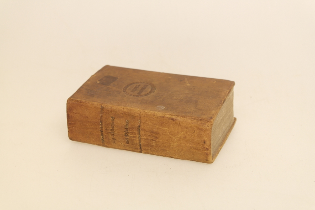 Bok i brunt skinn helbind, med trykte gullbokstaver på ryggen. Stempel trykket på forsiden.