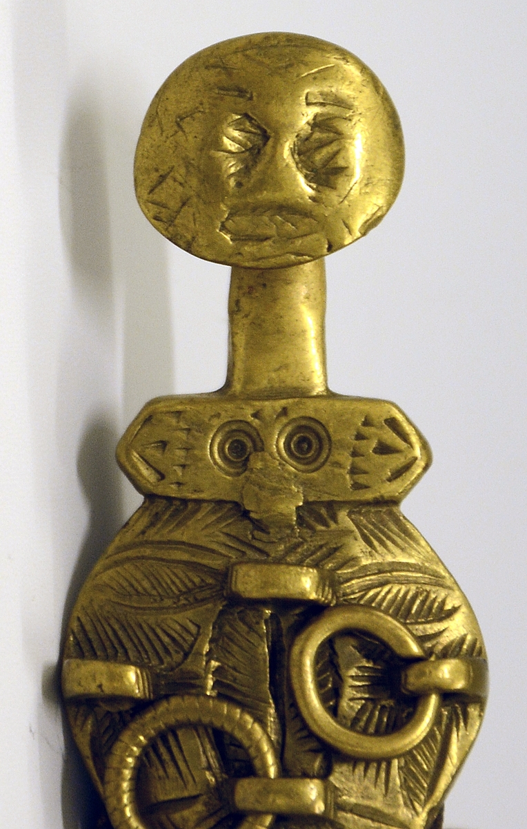 Slirehempe til belte og beltelås i messing. Fra protokollen: Bæltebeslag for tollekniver, av messing. Selve beslaget bestaar av a) 1 sprote (stolpelås eller beltelås) med paasatte 4-5 ringer og ornamenter i form av to masker.
b) En stolpe (slirehempe) med løkke paa. Fra stolpen gaar 2 par tvertagger, som gir plads til rembeslagene. Disse, der bestaar av 2 dobbeltbiøede plater ornerte med stjernepunkter, gaar rundt mellem tvertaggerne, og omslutter skindremmen som bokpermer. Beslaget har ringe og ornamenter.
