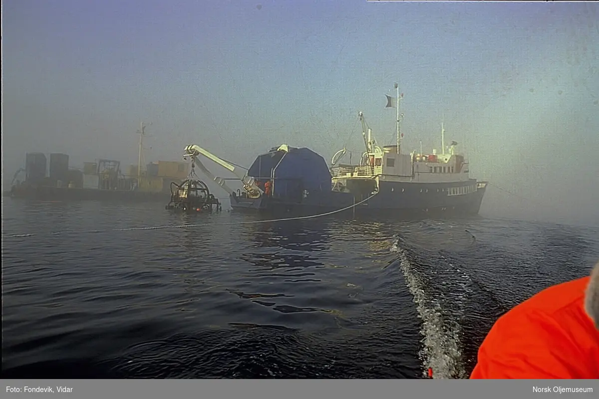 En mann kjører bort fra dykkerskipet "Strilborg" i en liten gummibåt.  Strilborg ble senere omdøpt til "Deepsea Inspector", og er moderskipet til miniubåten "Check Mate" som henger i kranbommen i akterenden av skipet.