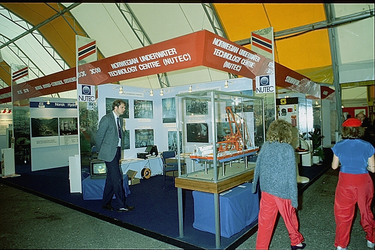 NUTEC sin stand på en messe. En person betjener standen.  En modell av "NUTEC Fjordbase" er plassert i en monter.