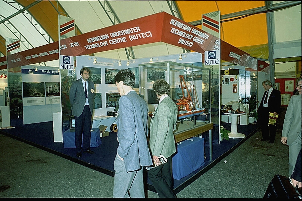 NUTEC sin stand på en messe. En person betjener standen.  En modell av "NUTEC Fjordbase" er plassert i en monter.