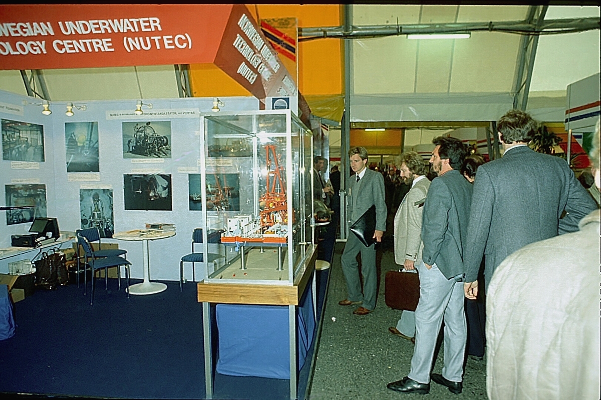 NUTEC sin stand på en messe. En person betjener standen.  En modell av "NUTEC Fjordbase" er plassert i en monter.