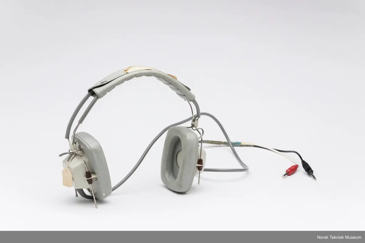 Hodetelefon med ledning og to plugger. Papirlapp festet til ene klokken med en tråd og tapebit på bøyle.