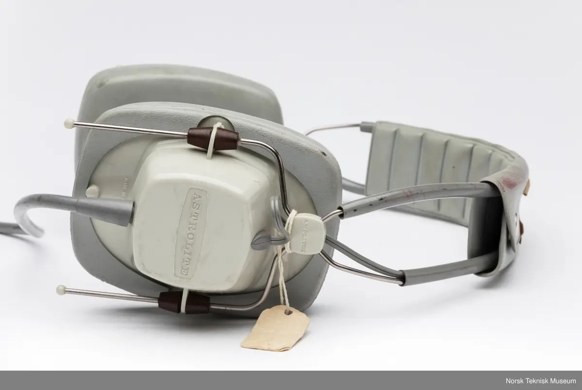 Hodetelefon med ledning og to plugger. Papirlapp festet til ene klokken med en tråd og tapebit på bøyle.