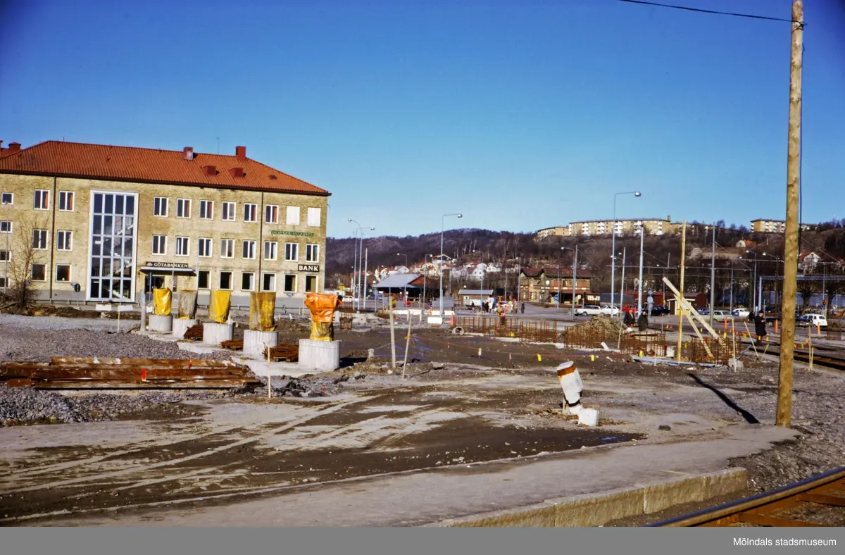 Byggnation av nya Mölndals Bro, ca 1974-1975. Till vänster ses Hantverkshuset med adress Frölundagatan 1/Kungsbackavägen 2, fasad mot Lillgatan. I mitten ses järnvägsstationen Mölndals Nedre och uppe på höjden bostadsbebyggelse i stadsdelen Enerbacken.