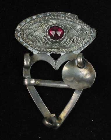 Hjertesprette av sølv med oval krone loddet til hjertet. Krona har tråddekor: fire trådspiraler lagt i s-form, stilt sammen parvis. Mellom disse er det en innfattet rubinrød fasettslipt glassperle (eller stein?) Dette feltet er begrenset av to trådbånd, det innerste av glatt tråd og det ytterste av tvinnetråd. Det er opprinnelig festet tre skåleløv til hjertegrinda, to mangler. Tornen er glatt og er festet på tvers av grinda. Flere stempler på baksida.