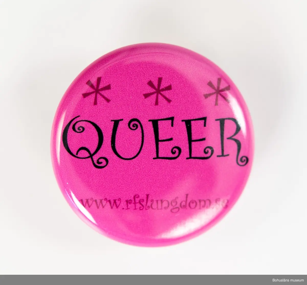 Runt rockmärke med nål för fastsättning på baksidan. 
Bakgrund i rosa med text: QUEER www.rfslungdom.se
[RFSL Ungdom - Ungdomsförbundet för HBTQ-personers rättigheter]
