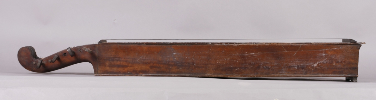 Korpus sammensatt av 4 bord, bunn og lokk limt på sidene. Lokk og bunnn i nåltre, sarger i løvtre. Hode og skruekasse i ett stykke - av løvtre. Hode i form av enkel snekke, 8 stemmeskruer. Sidene buket (Valdrestype), øvre fot mangler. 3 lydhull: 1 mindre grovt ovalt ved anslag (ant. etter kvist, (JV)), samt to par s-formet hull parvis speilvent (lager en hjerteform!).
Strengene festet i stifter like bak stol. Høyre sadel og forstykke festet til korpus med trenagler. Hele instrumentet er beiset mørk brunt. Skala på melodistrengen. Alle noter og pyramider mangler. Spor i lokket etter notene, ca 16 stk. Spor etter to strengeleder - gir korteste strenge ytterst.