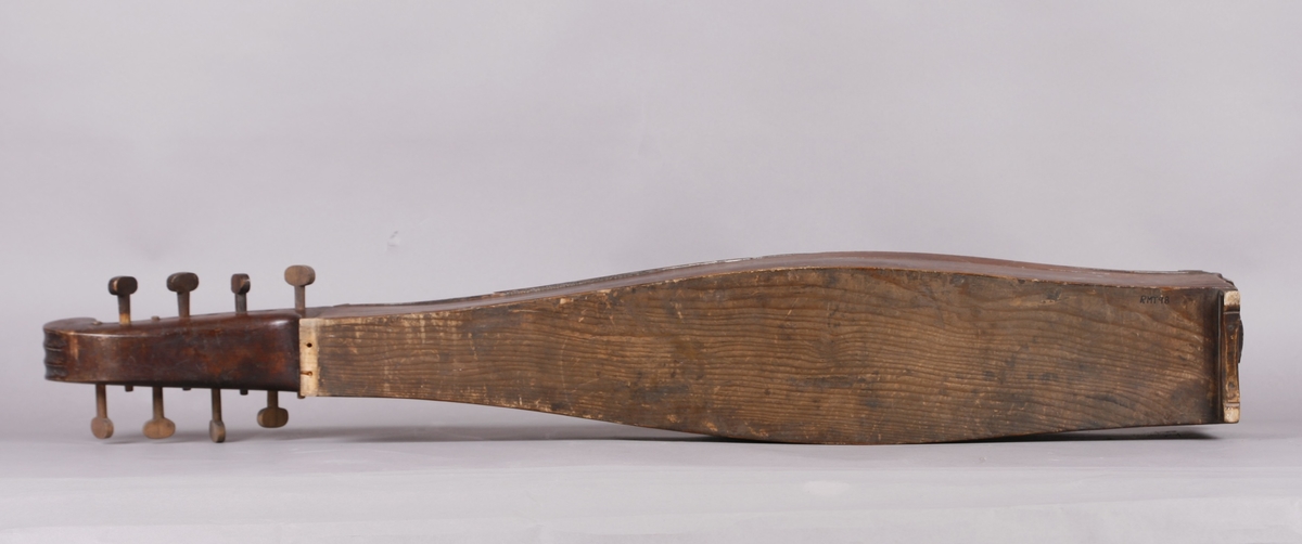 Korpus sammensatt av 4 bord, bunn og lokk limt på sidene. Lokk og bunnn i nåltre, sarger i løvtre. Hode og skruekasse i ett stykke - av løvtre. Hode i form av enkel snekke, 8 stemmeskruer. Sidene buket (Valdrestype), øvre fot mangler. 3 lydhull: 1 mindre grovt ovalt ved anslag (ant. etter kvist, (JV)), samt to par s-formet hull parvis speilvent (lager en hjerteform!).
Strengene festet i stifter like bak stol. Høyre sadel og forstykke festet til korpus med trenagler. Hele instrumentet er beiset mørk brunt. Skala på melodistrengen. Alle noter og pyramider mangler. Spor i lokket etter notene, ca 16 stk. Spor etter to strengeleder - gir korteste strenge ytterst.