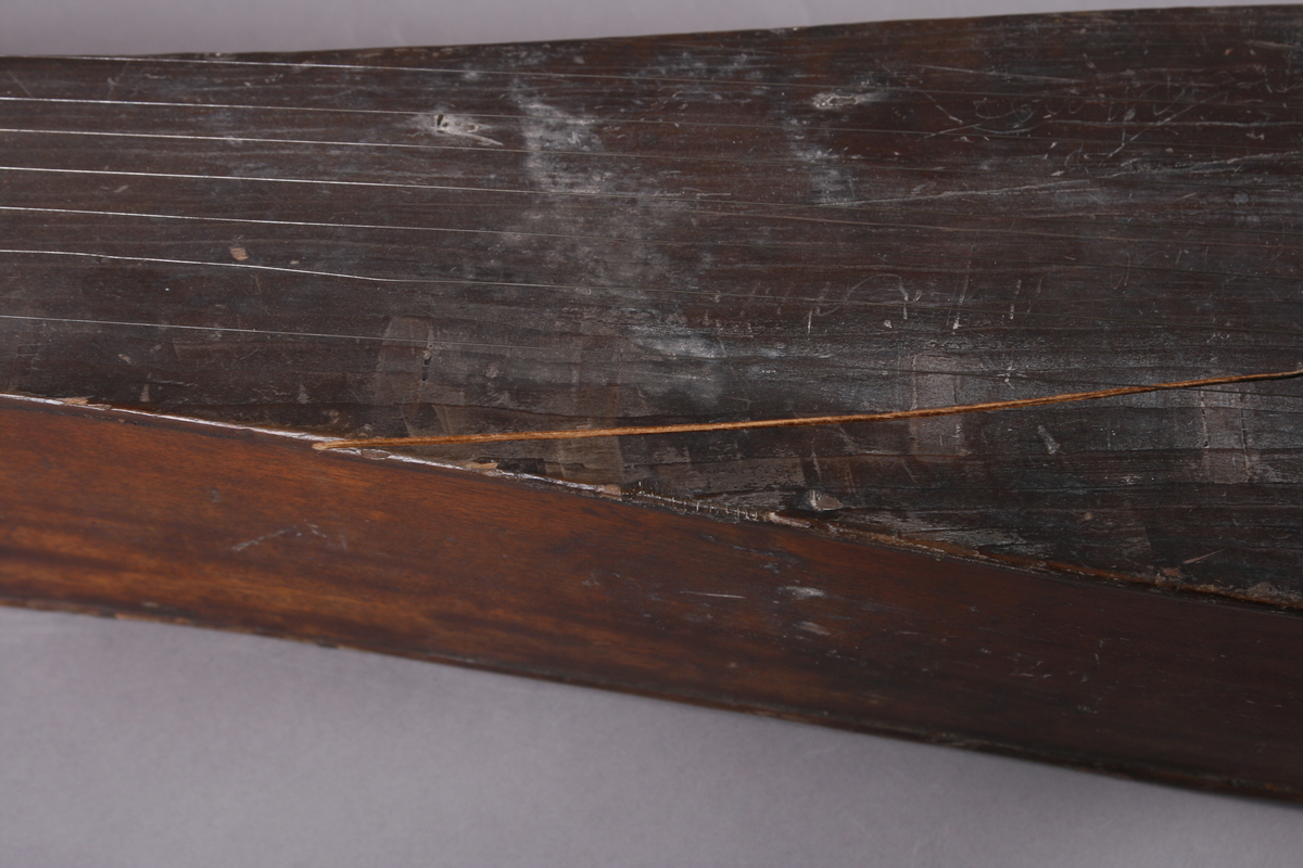 Korpus sammensatt av 4 bord, bunn og lokk limt på sidene. Lokk og bunnn i nåltre, sarger i løvtre. Hode og skruekasse i ett stykke - av løvtre. Hode i form av enkel snekke, 8 stemmeskruer. Sidene buket (Valdrestype), øvre fot mangler. 3 lydhull: 1 mindre grovt ovalt ved anslag (ant. etter kvist, (JV)), samt to par s-formet hull parvis speilvent (lager en hjerteform!).
Strengene festet i stifter like bak stol. Høyre sadel og forstykke festet til korpus med trenagler. Hele instrumentet er beiset mørk brunt. Skala på melodistrengen. Alle noter og pyramider mangler. Spor i lokket etter notene, ca 16 stk. Spor etter to strengeleder - gir korteste strenge ytterst.